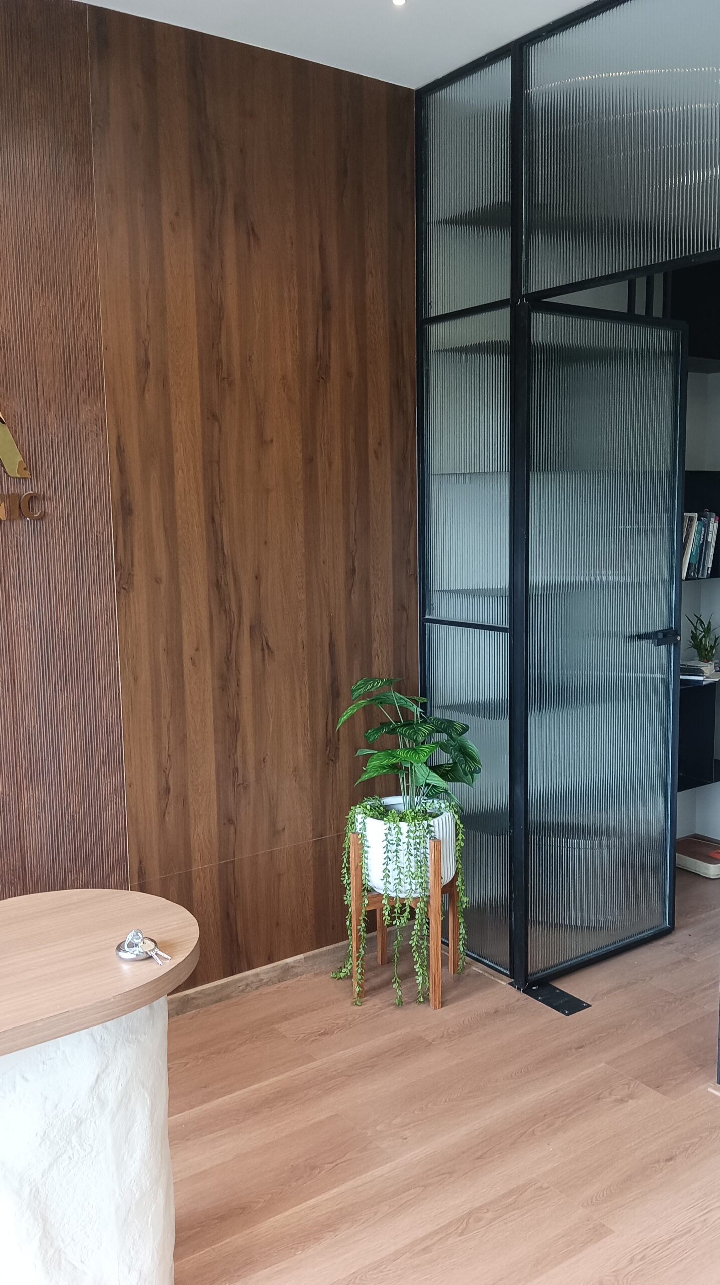 Office interior with a long white meeting table, light wood shelving mounted on vertical wood‑paneled wall, green task chairs, soft overhead lighting.