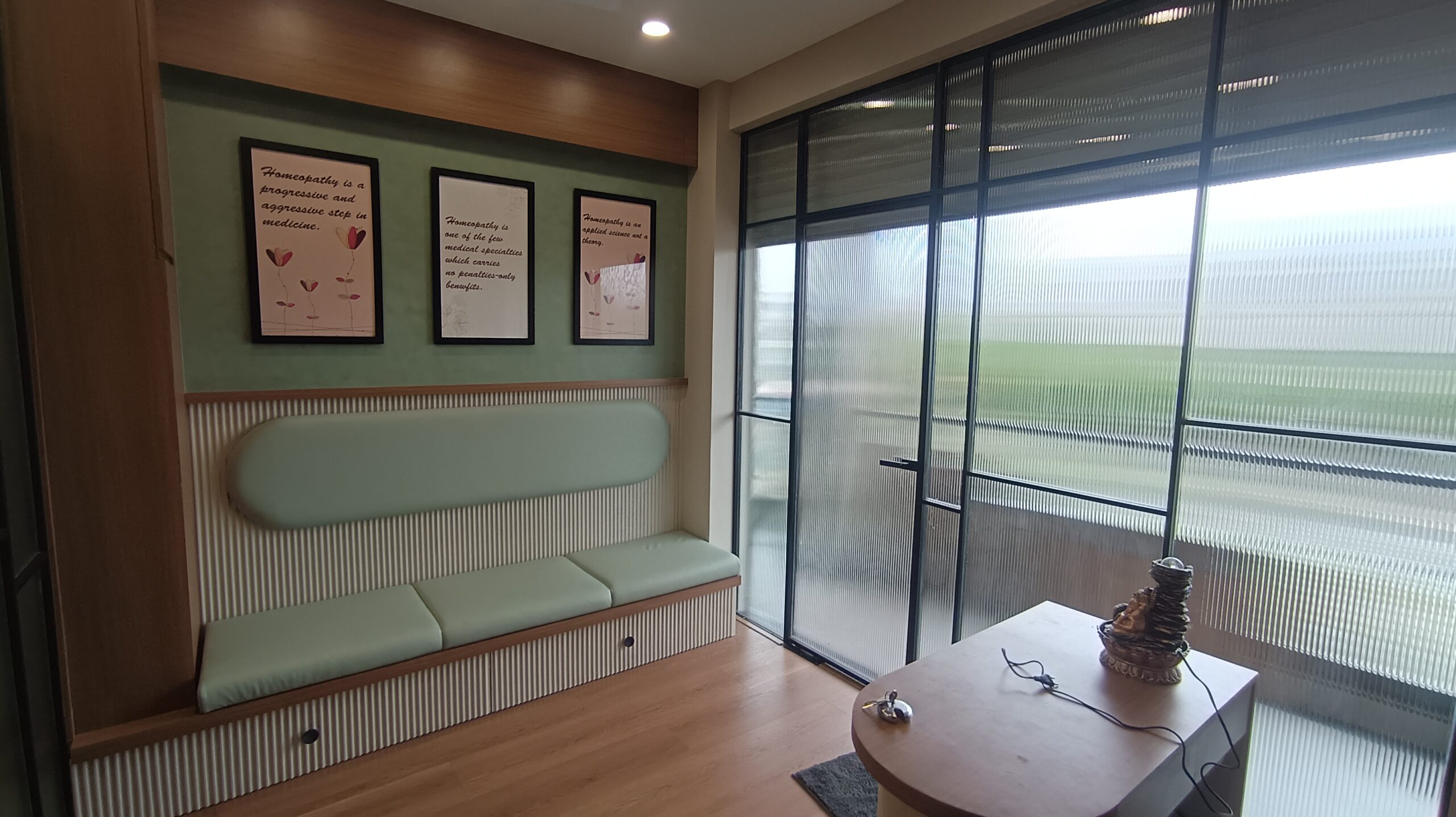 Office area with modular shelves, a long wooden desk, green chairs, and neutral decor; lit with daylight from a window.