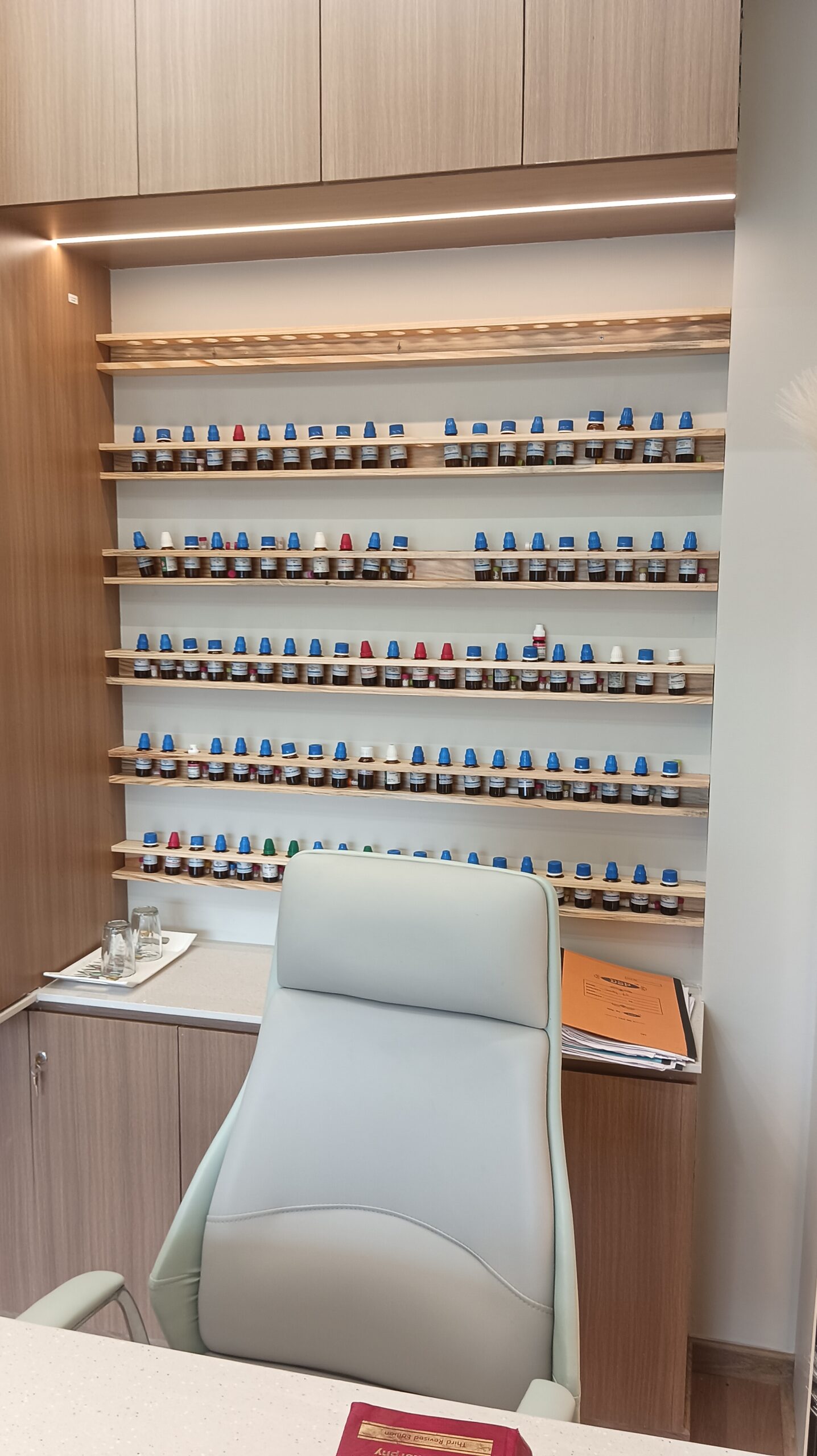 Open lounge corner with a low upholstered bench, vertical black metal divider panels, light wood flooring, and soft green accent wall.