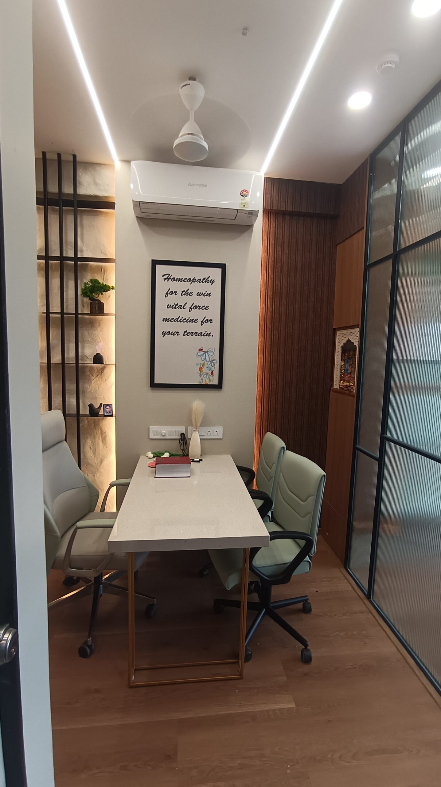 Office hallway featuring glass partition walls, suspended pendant lighting, light-colored flooring, and a clean, modern aesthetic.