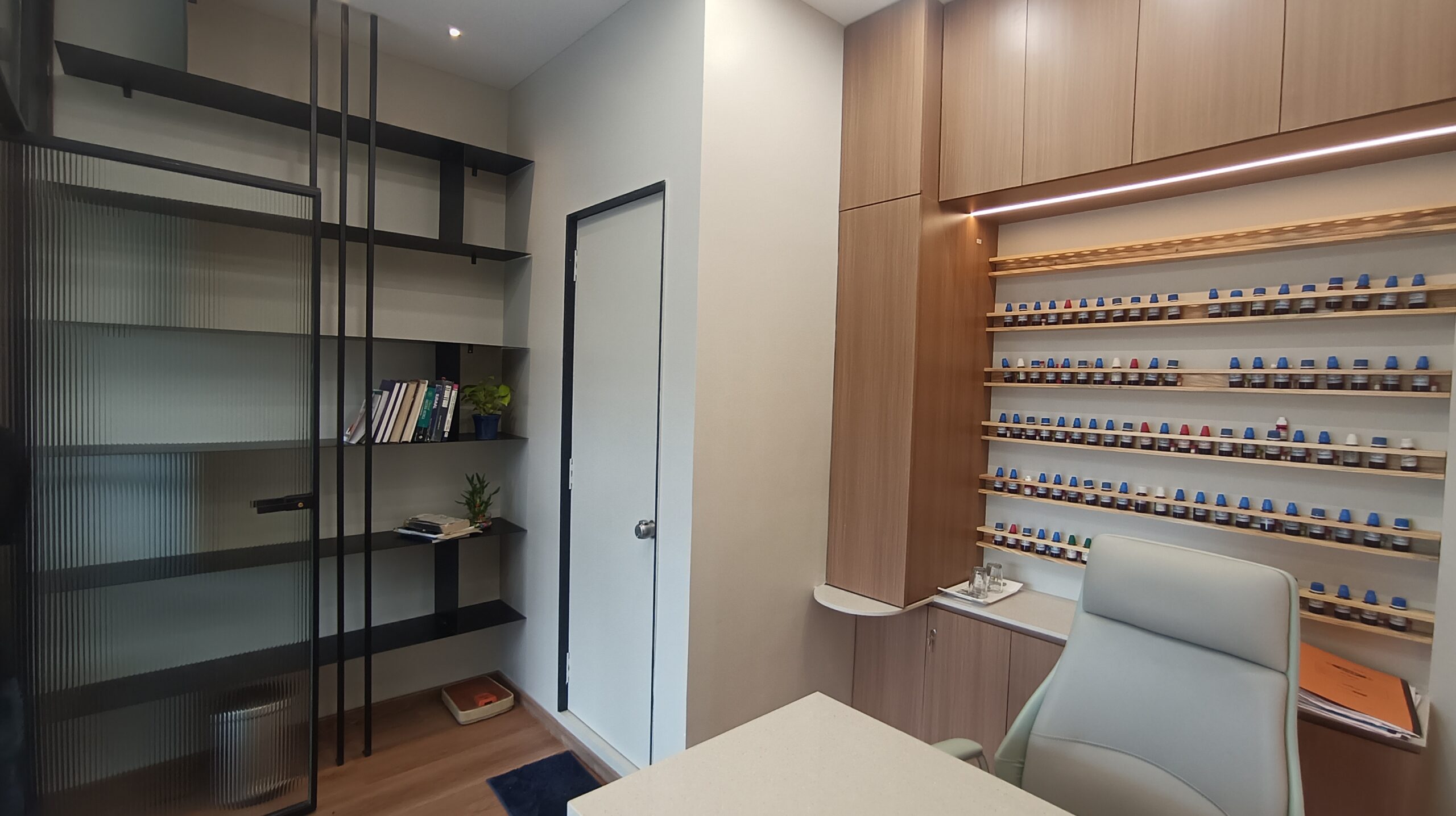 Simple office workspace featuring a wooden desk, potted green plants, natural light from windows, and a clean, uncluttered environment.