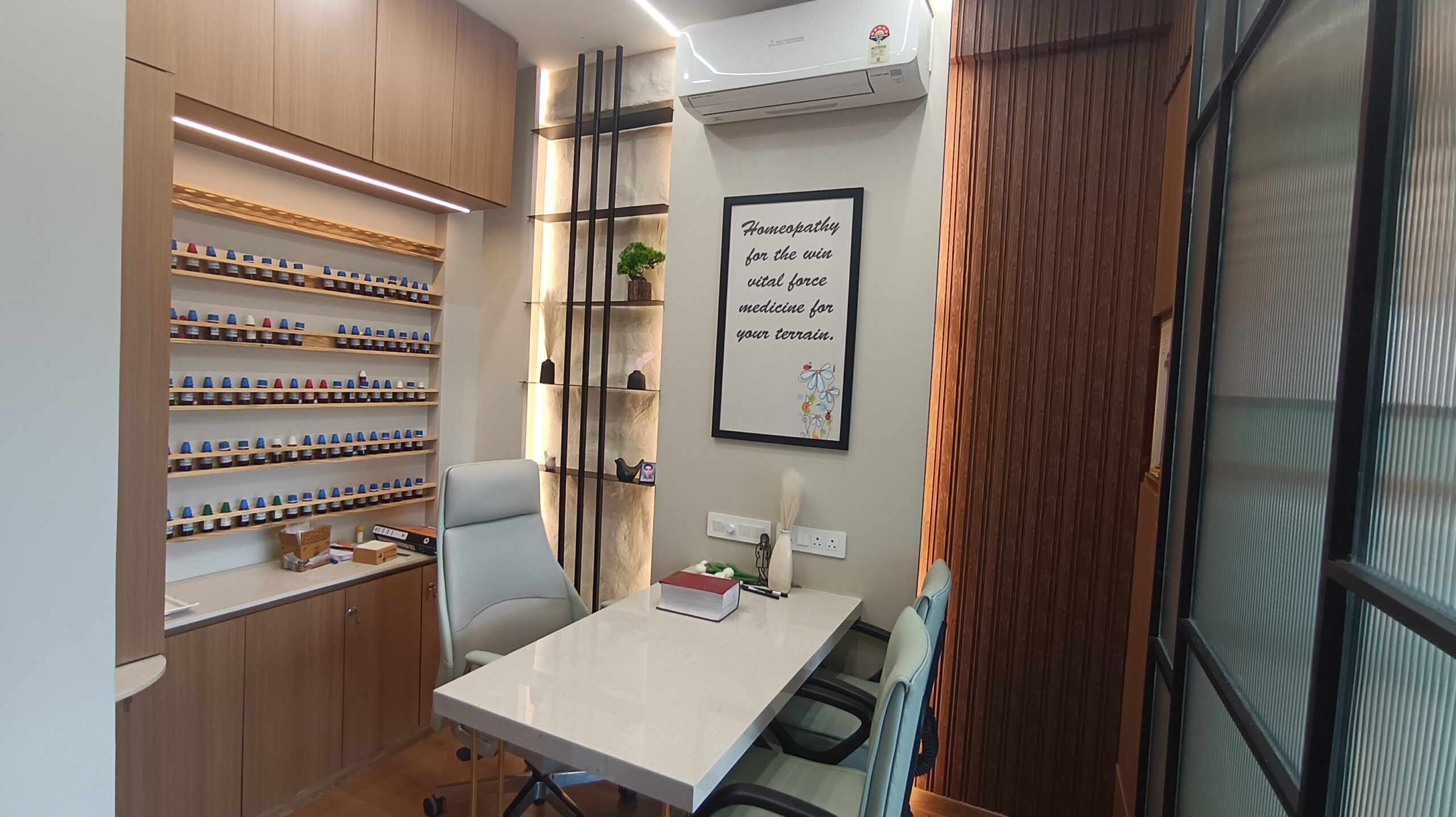 Office lounge area featuring white modern chairs, small round tables, green plants, and natural light from large windows.