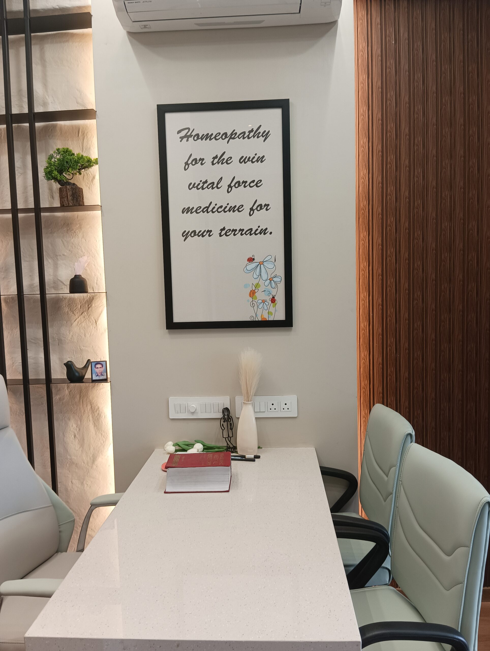 Open office area featuring wooden desks with built-in shelving, task chairs, pendant lighting, and natural light from large windows.