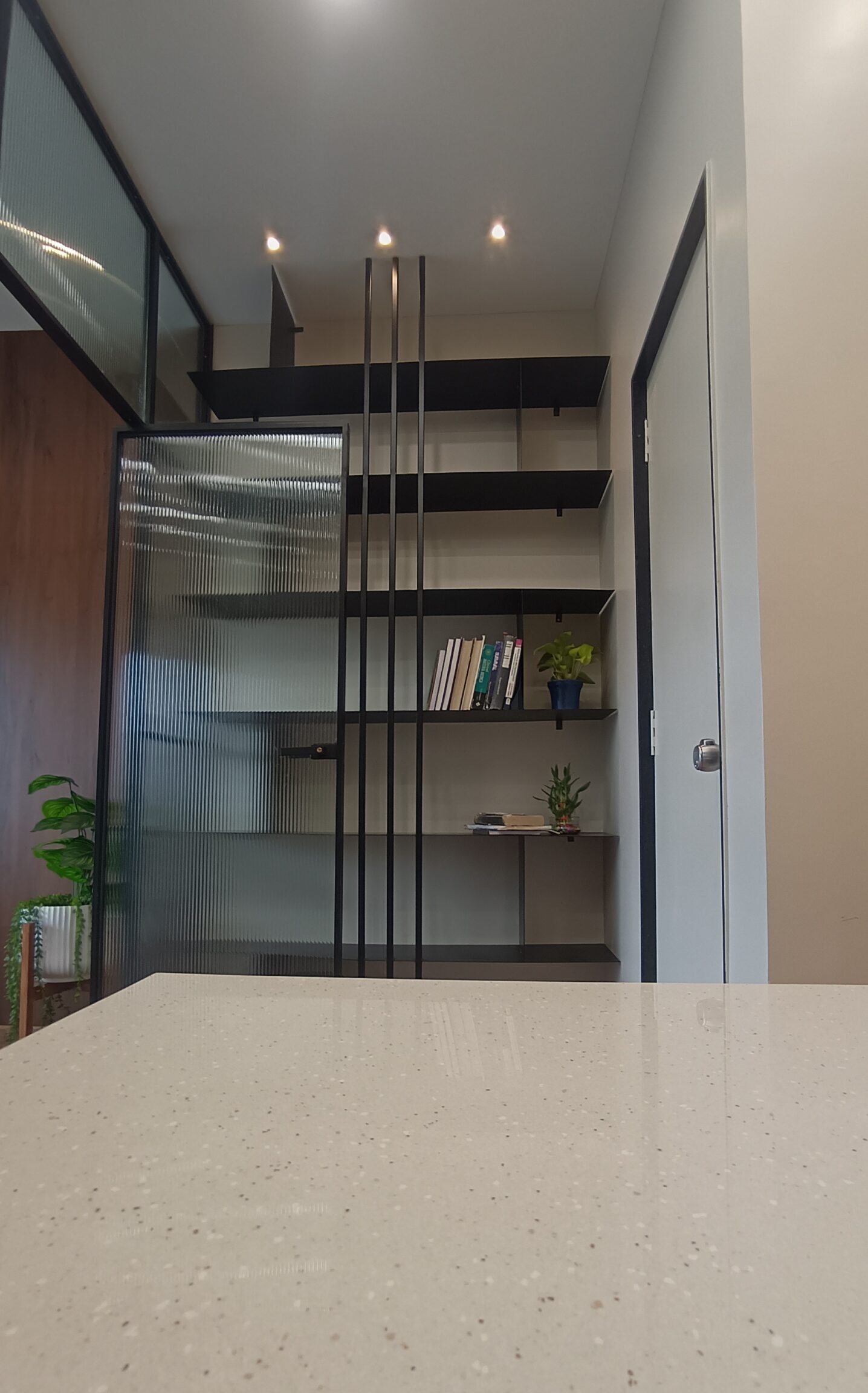 Minimalist office kitchenette featuring light wood cabinetry, white countertops, a stainless steel sink, and modern appliances in a bright setting.